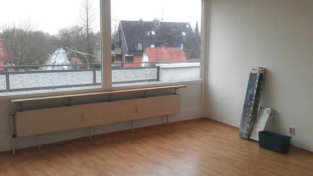 ein nicht müblierter raum, mit hellem holzboden und einer fensterfront, an der wand lehnen kartons